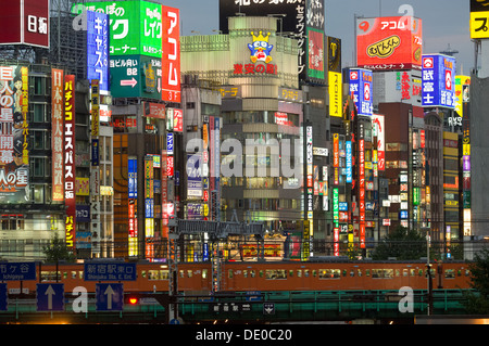 Train passing buildings lit with neon advertising signs, Shinjuku District, Tokyo, Japan Stock Photo