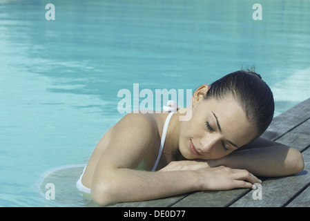 Woman in pool leaning against deck, resting head on arms Stock Photo