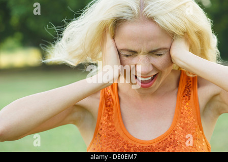 Woman screaming with eyes closed and hands over ears Stock Photo