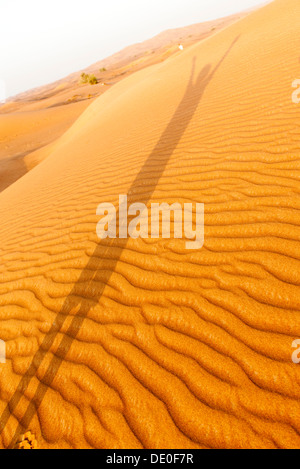 Shadow of person with arms raised cast on desert sand Stock Photo