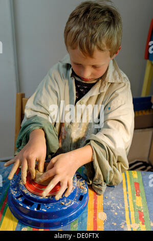 Little boy, 7, making pottery, turning a jar from clay on a potter's wheel Stock Photo