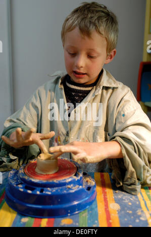 Little boy, 7, making pottery, turning a jar from clay on a potter's wheel Stock Photo