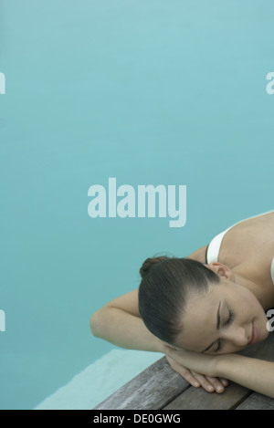 Woman lying next to pool, resting head on arms, eyes closed Stock Photo