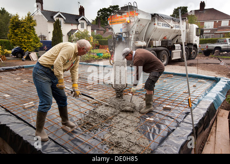 self building house, pouring readymixed concrete steel mesh reinforced prepared floor slab, two men raking level Stock Photo