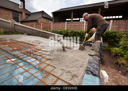 self building house, pouring readymixed concrete steel mesh reinforced prepared floor slab, two men raking level Stock Photo