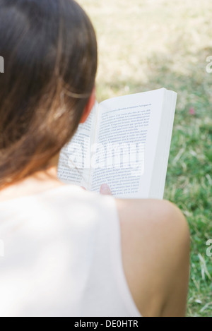 Woman reading book outdoors, over the shoulder view Stock Photo
