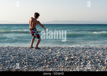 Teenage boy throwing stones into sea Stock Photo