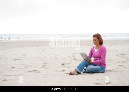 Woman sitting with an iPad on a beach Stock Photo