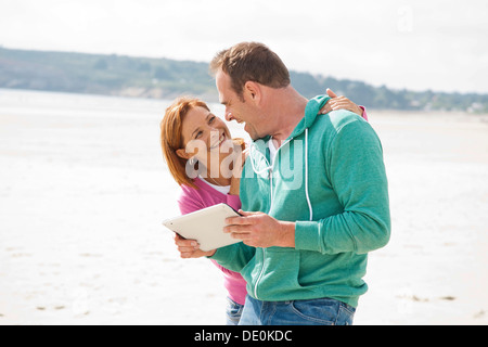 Couple playing with an iPad on a beach Stock Photo
