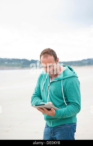Man playing with an iPad on a beach Stock Photo