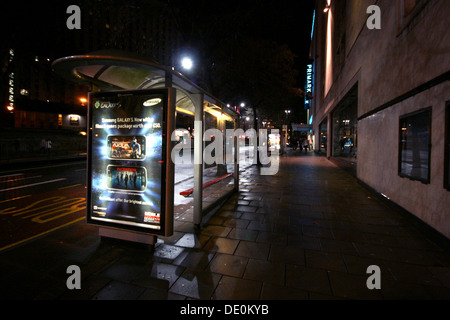 An urban scene showing a bus stop in the heart of the city at night. Stock Photo