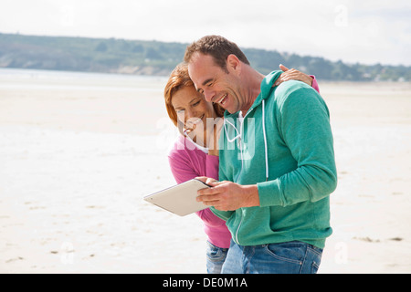 Couple playing with an iPad on a beach Stock Photo