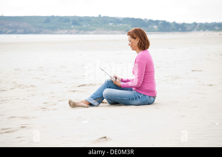 Woman sitting with an iPad on a beach Stock Photo