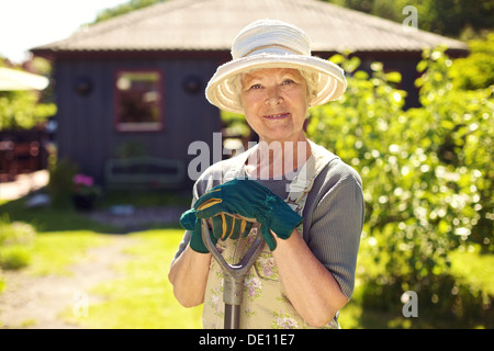 Portrait of elder woman with gardening tools outdoors. Senior woman standing with shovel in her backyard Stock Photo