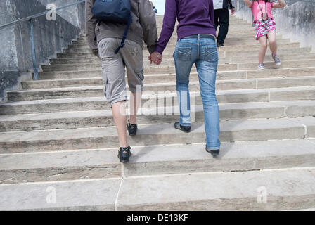 Young couple going up the stairs together, hand in hand, from behind Stock Photo