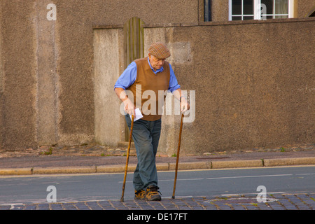 Old man with walking sticks, crossing the road to post a letter. Northern England. Stock Photo