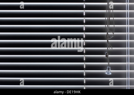 Shutter blind closed, light seeping through, pull cord visible. Stock Photo