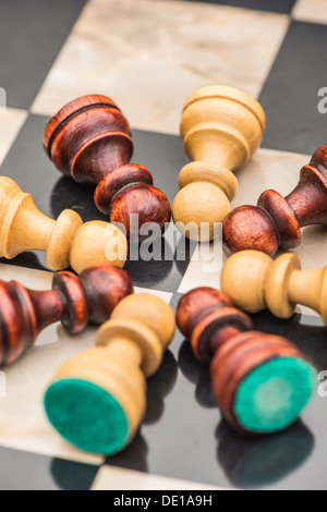 Closeup of chess pieces, white and black pawns lying on chessboard representing teamwork. Stock Photo