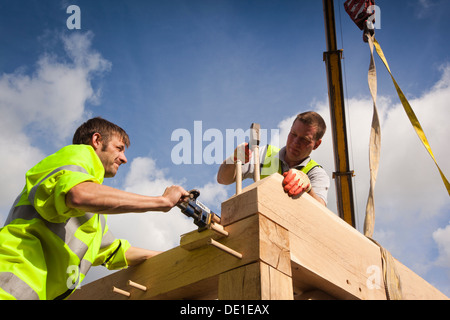 self building house, constructing green oak timber framed garage, pegging frame, whist crane lifts heavy structure Stock Photo