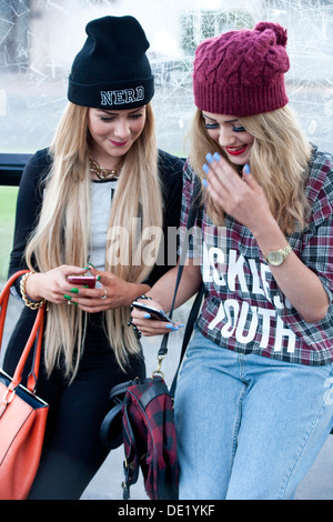 Two teens sitting at a bus stop having fun with their mobile phones. Stock Photo