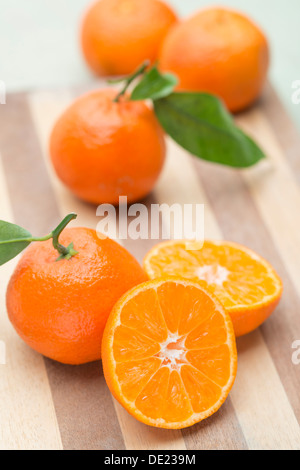 A nice still life arrangement of Seville oranges with green leaves on a wooden chopping board Stock Photo