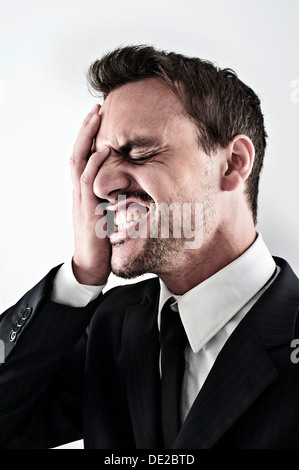 Desperate young man wearing a suit covering his face with his hand, screaming Stock Photo