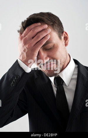 Young man wearing a suit holding his hand on his forehead, worried Stock Photo