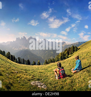 Hikers relaxing in a meadow enjoying the view of the Geisler group, Aferer Geisler mountains, Villnoesstal valley Stock Photo