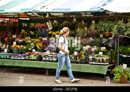 Young woman walking pass a market stall and looking at plants flowers for sale, Cambridge, England Stock Photo