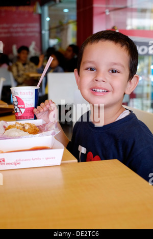 happy little boy of mixed race enjoying a chicken meal at kfc in malang java indonesia Stock Photo