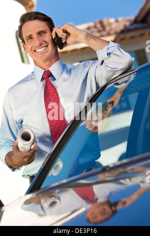 A successful businessman or architect holding plans & talking on his cell phone by a car Stock Photo