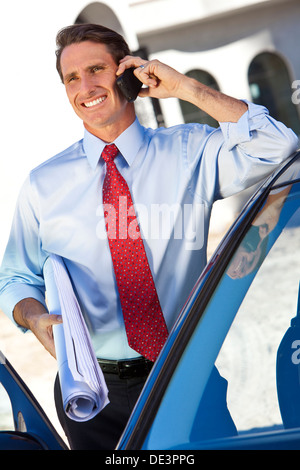 A successful businessman or architect holding plans & talking on his cell phone by a car Stock Photo