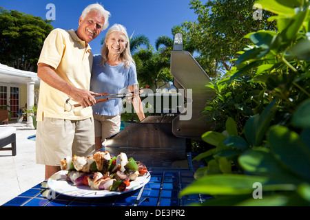 Happy senior man and woman couple outside cooking kebabs on a summer barbecue Stock Photo