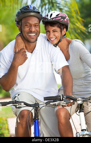 A happy laughing young African American couple with big smiles riding their bicycles outside Stock Photo