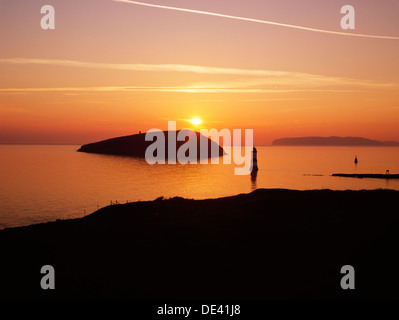 Penmon, Anglesey: Penmon Point lighthouse, Perch Rock & Puffin Island at sunrise, looking ENE across Conwy Bay to the Great Orme at Llandudno. Stock Photo