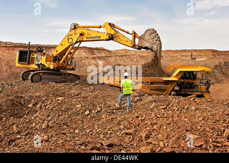 Supervisor overseeing gold mine operation in open cast surface pit with excavator and haul truck working, Mauritania, NW Africa Stock Photo