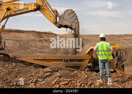 Supervisor overseeing gold mine operation in open cast surface pit with excavator and haul truck working, Mauritania, NW Africa Stock Photo