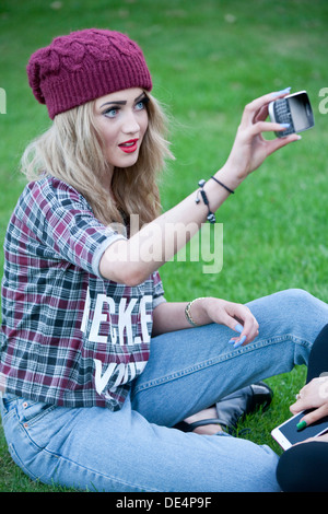 Blond teenage girl sitting outside taking a self portrait on her phone. Stock Photo