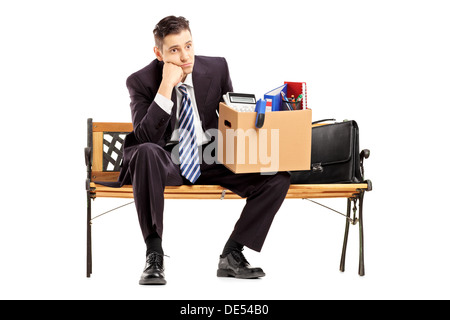 Disappointed redundant businessman in a suit sitting on a bench with a box of belongings Stock Photo