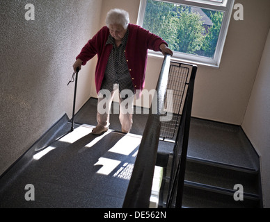 Independent elderly senior pensioner lady at 99 years climbing two flights of stairs aided only by her walking stick Stock Photo