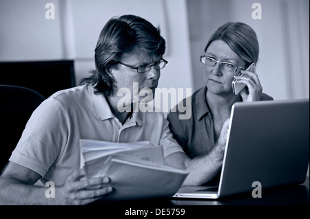 Worried mature couple at home working on their laptop computer dealing with serious financial issues ( B&W RGB toned conversion) Stock Photo