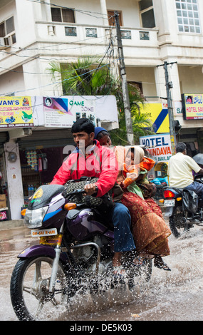 Indian family on a motorcycle riding through wet flooded streets in Puttaparthi, Andhra Pradesh, India Stock Photo