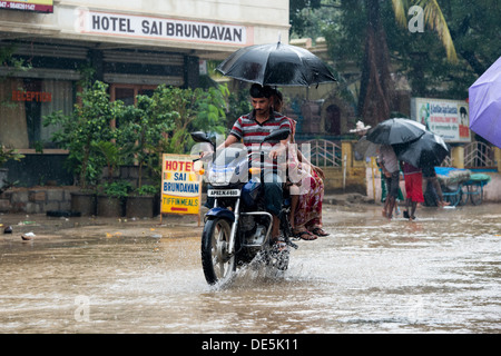 Indian family on a motorcycle with umbrella riding through wet flooded streets in Puttaparthi, Andhra Pradesh, India Stock Photo