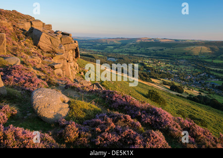 Heather surrounds a millstone on Bamford Edge with the village of Bamford below. Peak District, Derbyshire, England Stock Photo