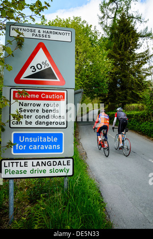 Cyclists pass warning signs in Little Langdale in the English Lake District Stock Photo