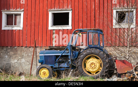 Small blue tractor stands on grass nearby red barn wall in Norway Stock Photo