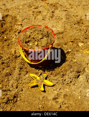 A child's sand filled bucket and yellow plastic starfish on the beach Stock Photo