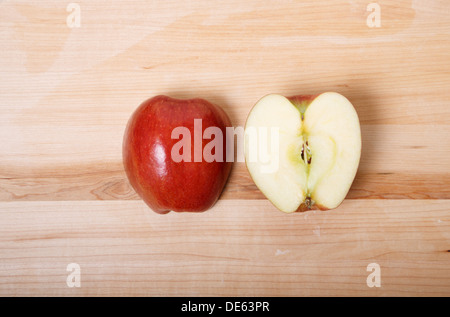 A red apple cut in half on a wood cutting board with skin side and cut side up Stock Photo
