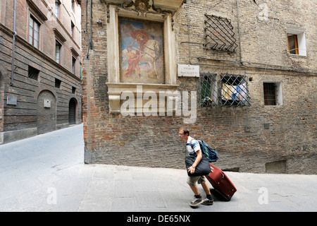 Sienna, Tuscany, Italy. Tourist on Vicolo Magalotti street in mediaeval city centre carrying baggage on his way from to hotel Stock Photo