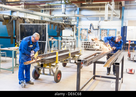 In an industrial setting, two workers craft and hone the metal extrusions for a construction project. Stock Photo